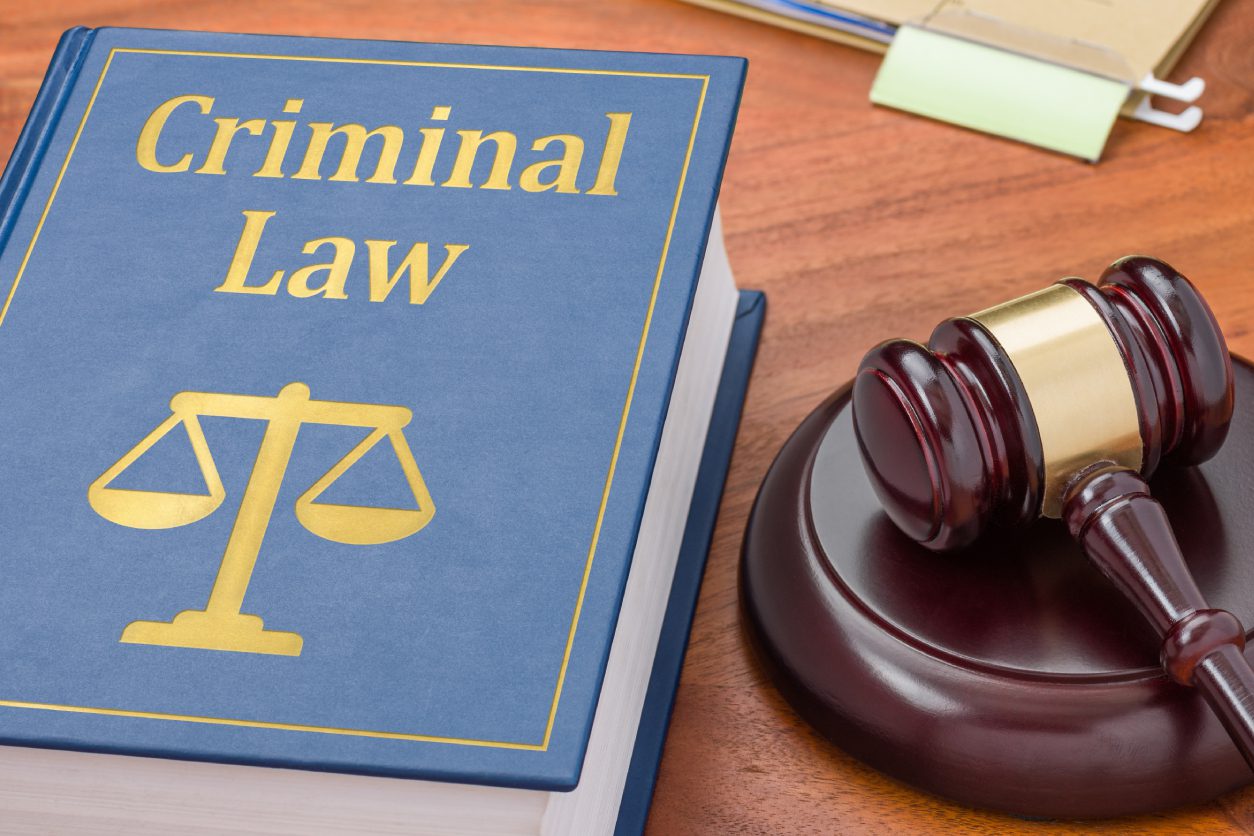 A criminal law book with justice scales on the cover is next to a wooden gavel on a table.