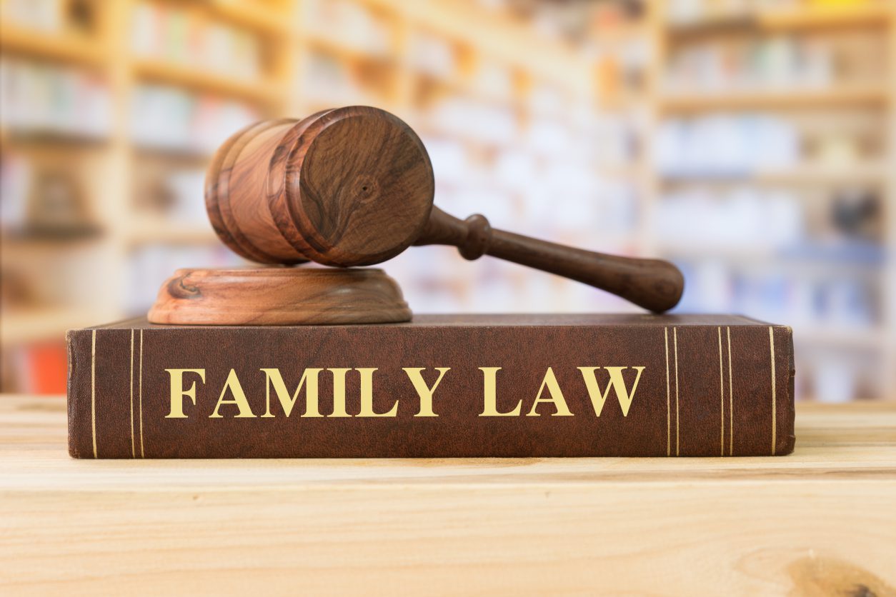 A wooden gavel rests on a "Family Law" book against a blurred background of shelves.